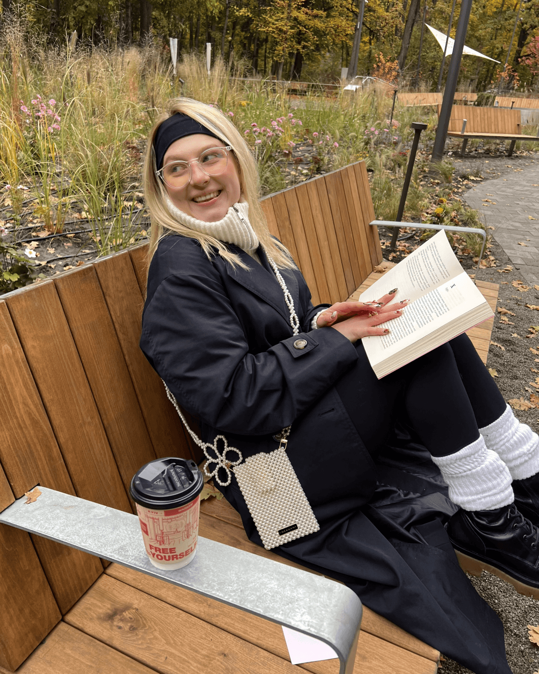 Дівчина на лавочці з книжкою, бісерним чохлом і кавою